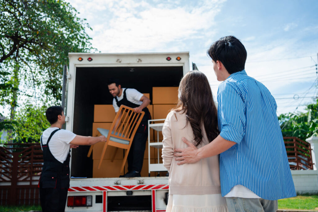 couple watching movers unload moving truck at new home